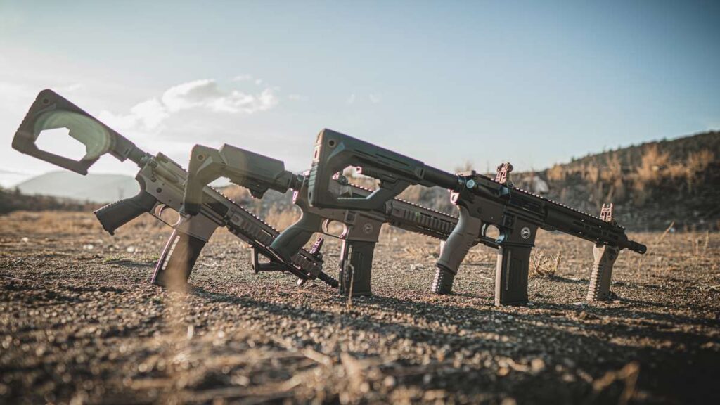 Three AR-15 rifles with polymer stocks and grips standing in a row at a range